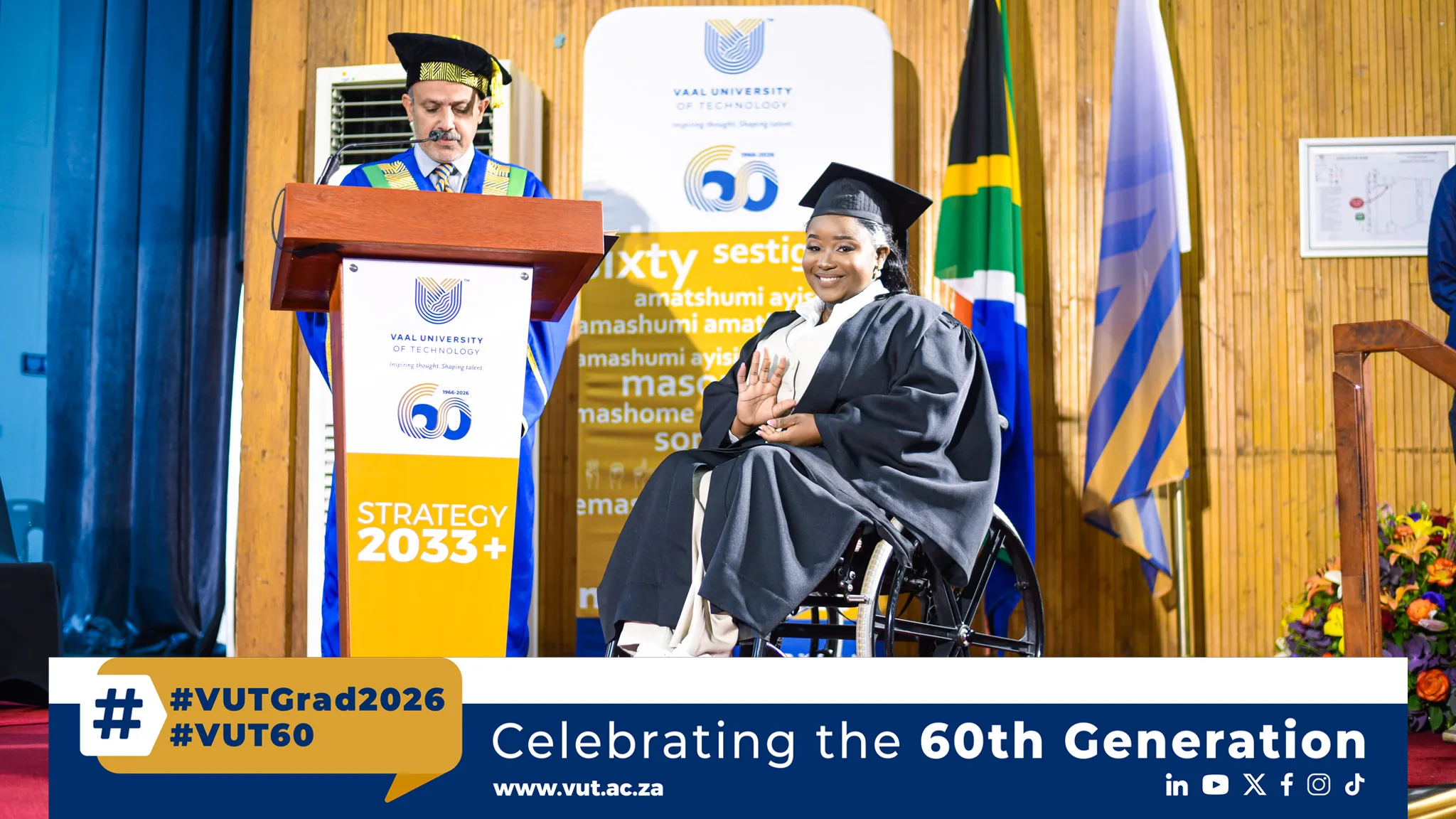 Simango Masungulo – Vaal University of Technology Graduate in a wheelchair smiles on stage during a Vaal University of Technology ceremony with a speaker at the podium nearby.