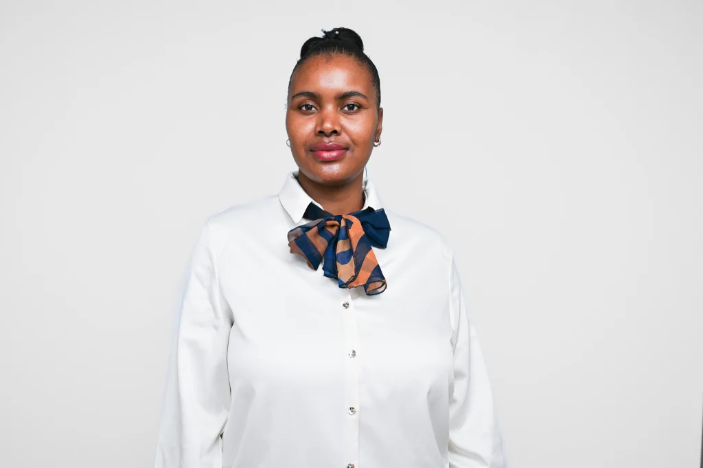 Portrait of a woman facing the camera wearing a white blouse and a blue‑orange striped neck scarf tied in a bow at the collar