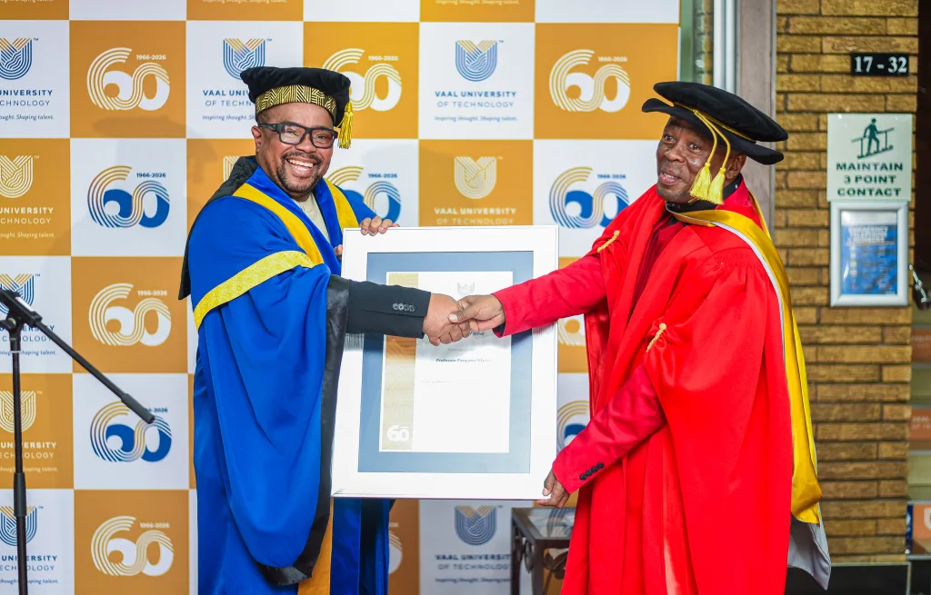 Professor Fanyana Mtunzi – Vaal University of Technology Two graduates in blue and red academic regalia shake hands while exchanging a framed certificate at a 60th anniversary ceremony, with logos in the background.