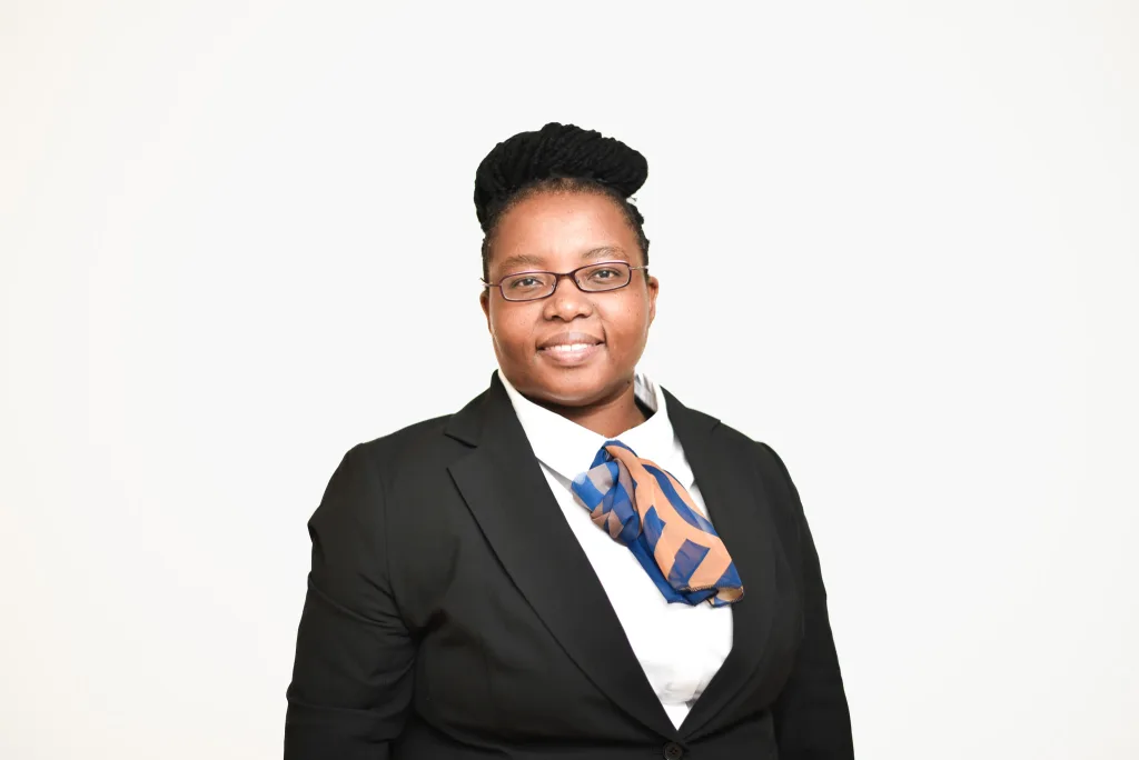 Professional woman in a black blazer with a blue and orange scarf, smiling at the camera against a white background, wearing glasses.