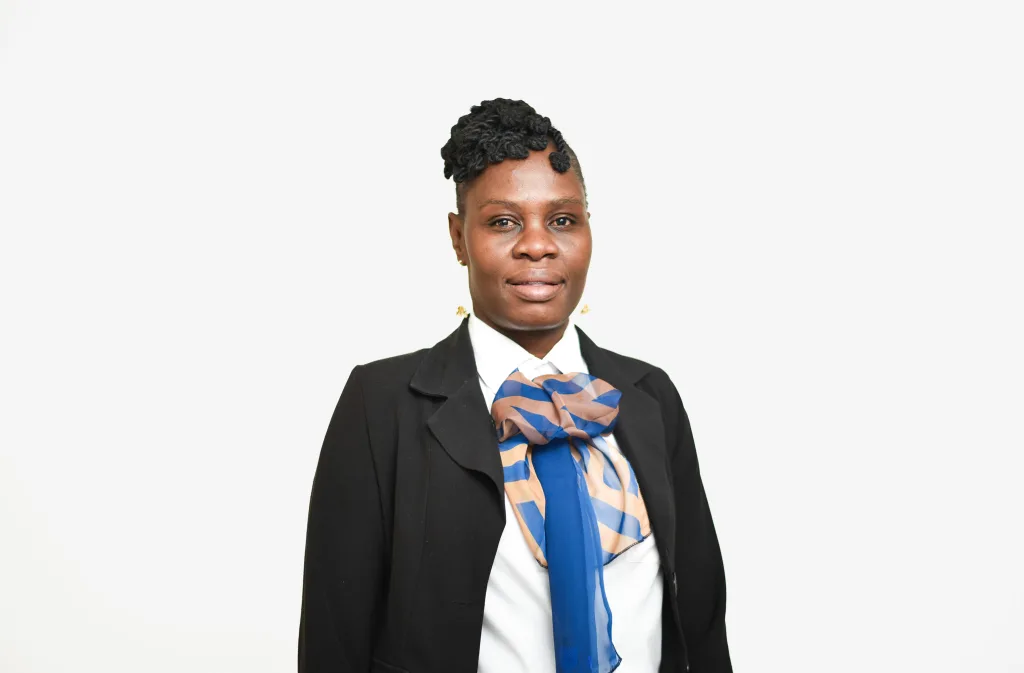 Portrait of a person wearing a black blazer, white shirt, and blue and peach scarf against a light background, facing the camera.