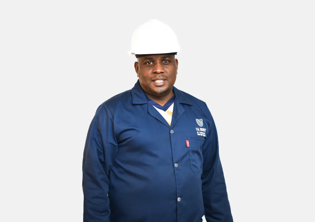 Male construction or industrial worker wearing a white hard hat and blue coveralls, facing the camera with a slight smile.