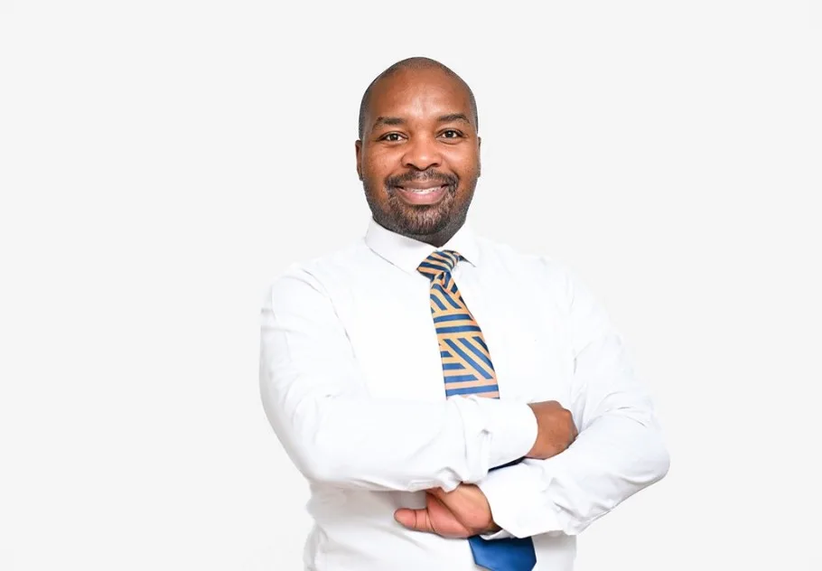 Professional portrait of a smiling man with arms crossed, wearing a white shirt and striped tie against a light background.