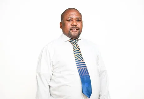 Portrait of a man in a white shirt and striped blue tie standing against a white background.