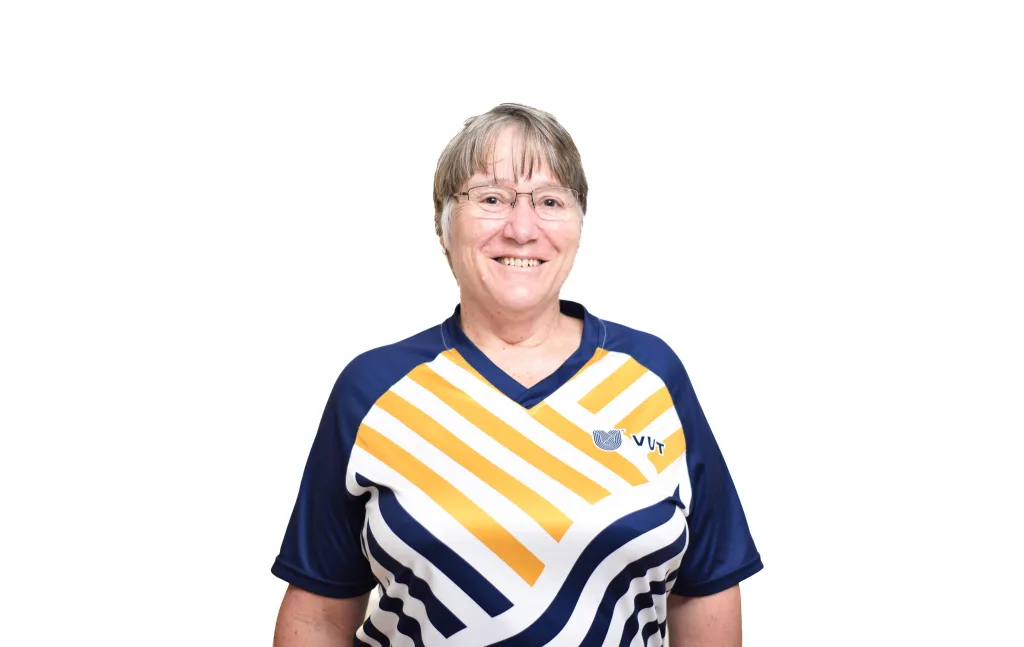 Smiling woman with short gray hair and glasses, wearing a blue and yellow diagonal-striped sports jersey against a white background.