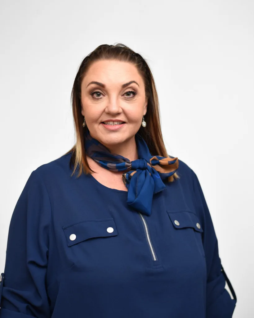 Portrait of a smiling woman in a navy blouse with a blue scarf tied at the neck.
