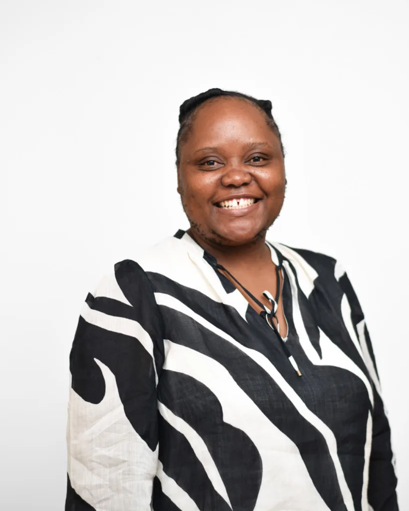 Smiling woman facing the camera in a bold black-and-white zebra-patterned blouse against a white background (portrait).