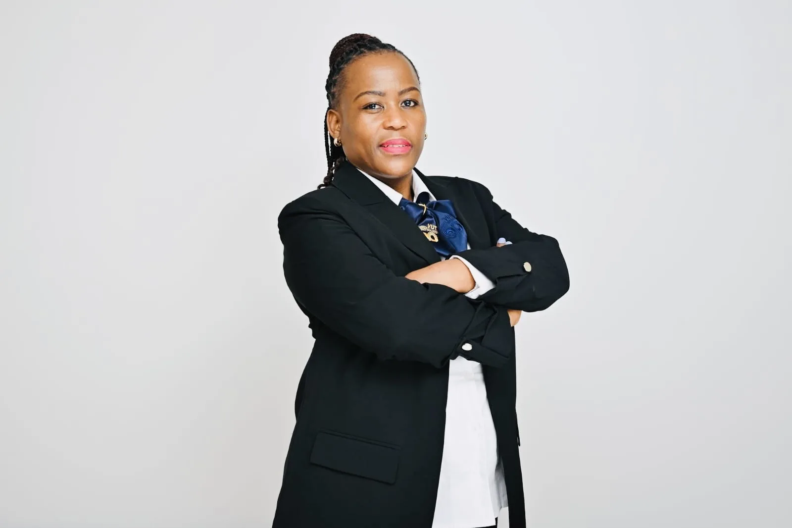 Professional woman in a black blazer and white shirt with arms crossed, posing confidently against a light gray background.