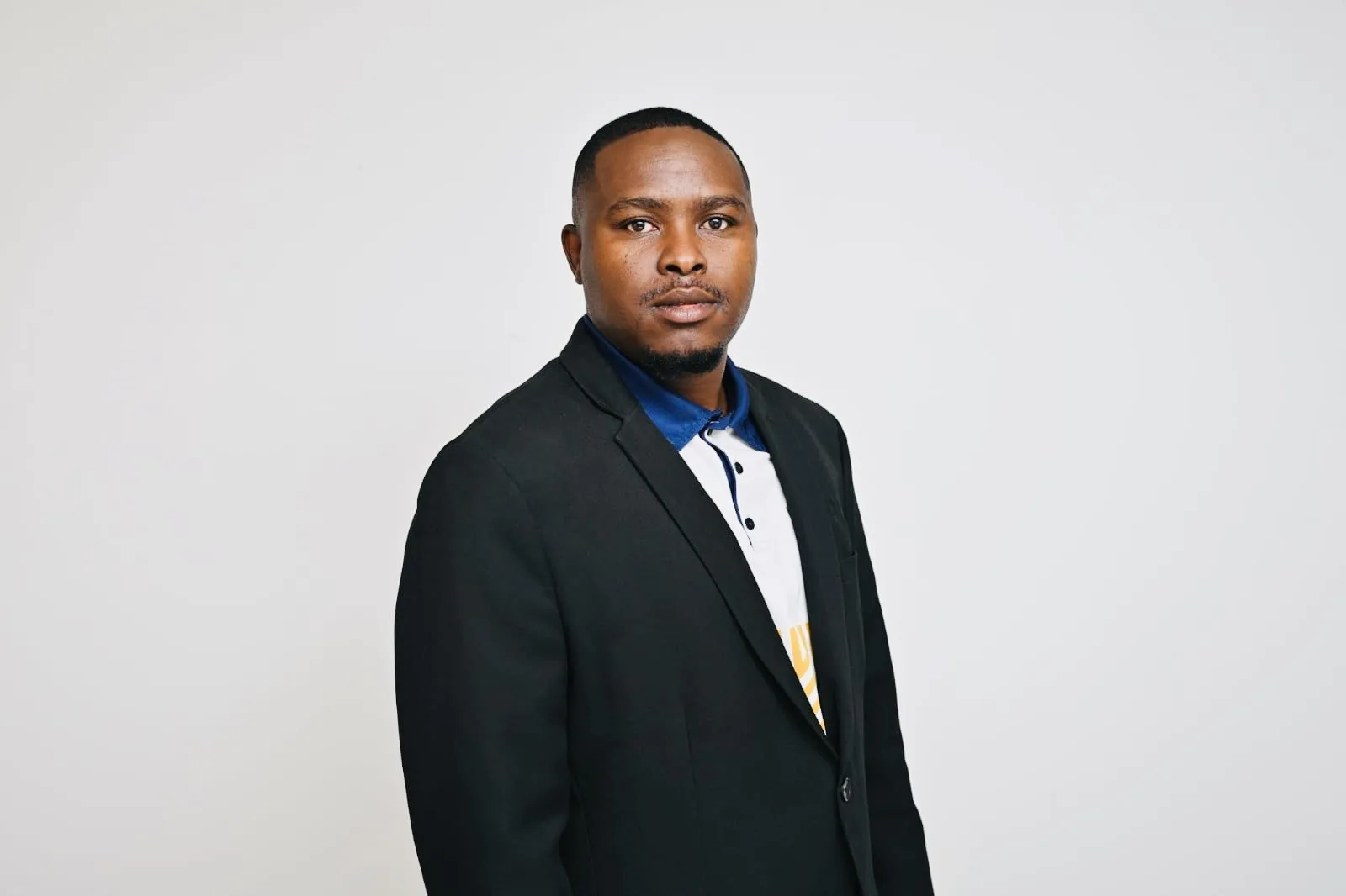 Professional headshot of a man in a black blazer and blue shirt against a neutral gray background, facing the camera.