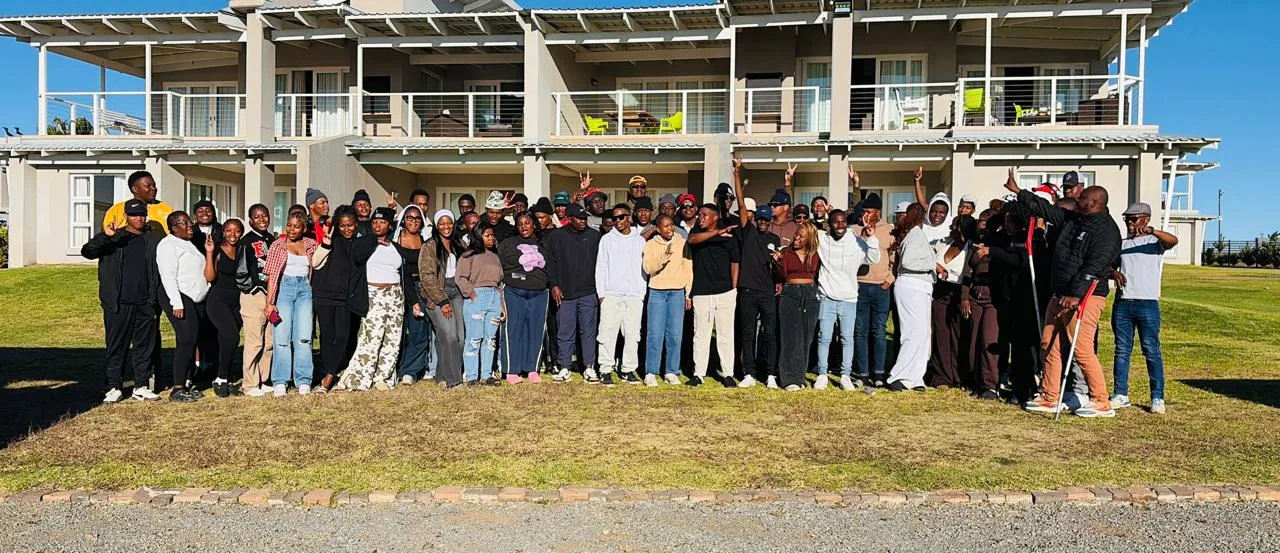 VUT Staff members – Vaal University of Technology – Vaal University of Technology Large diverse group posing for a photo on a lawn in front of a two-story building with balconies.