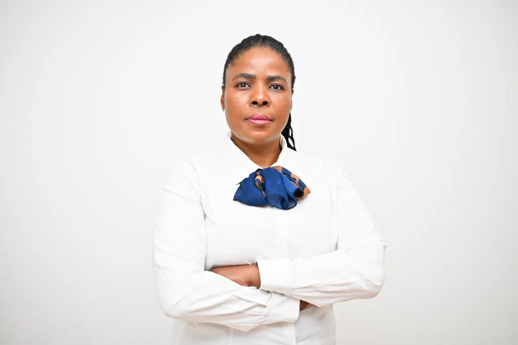 Professional woman with arms crossed, wearing a white shirt and blue scarf, facing the camera.
