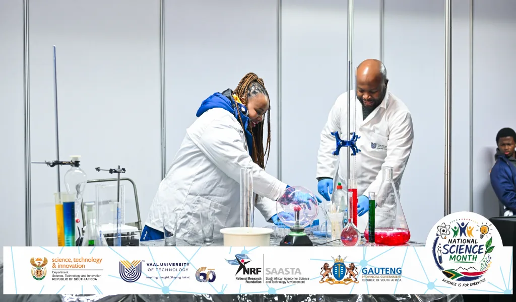 UT brings Science to life at National Science Month 2026 launch – Vaal University of Technology Two scientists in white lab coats work at a laboratory bench with glassware and colorful liquids, conducting an experiment during a science event.