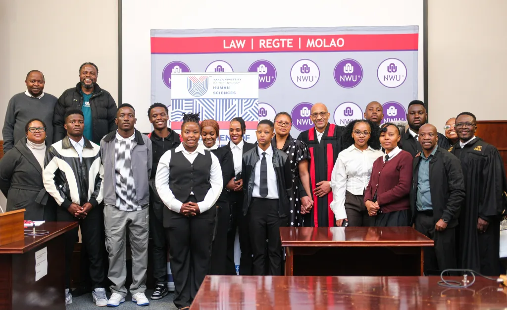 Moot court – Vaal University of Technology Group photo of a diverse group of students and faculty in robes and formal attire posing in a room with a Law banner and NWU logos in the background.