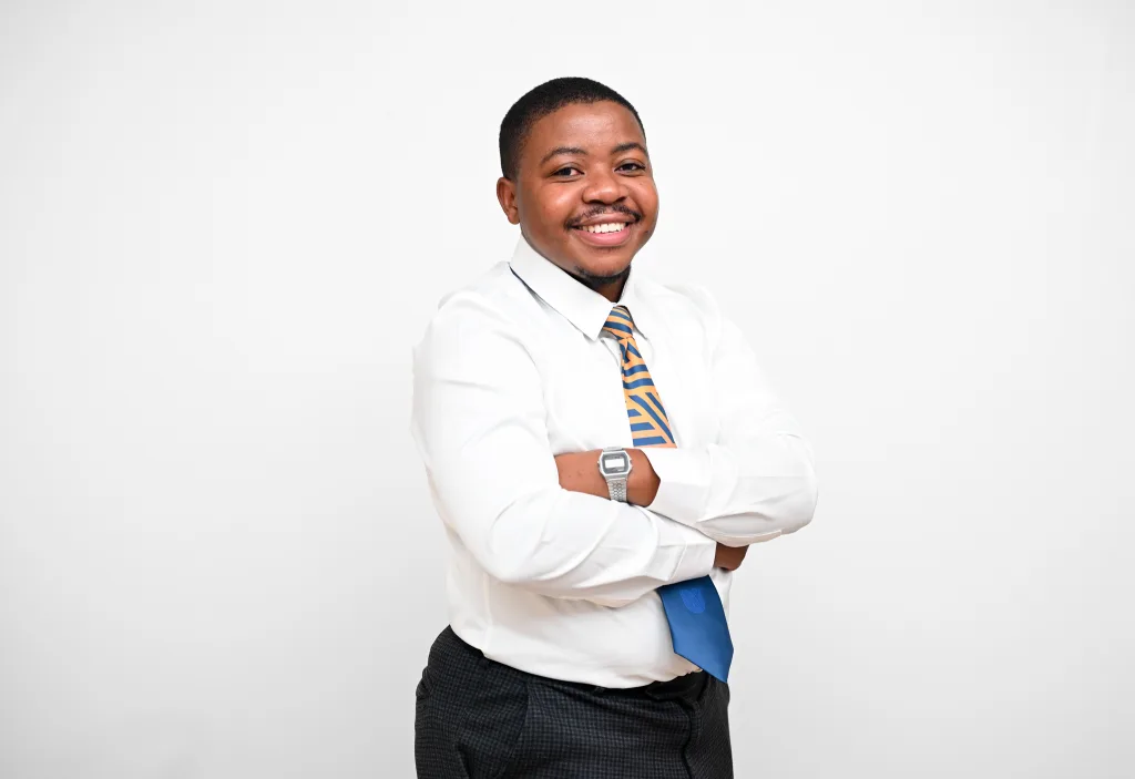 Young man in a white dress shirt and orange-blue striped tie, arms crossed, smiling against a plain white background.