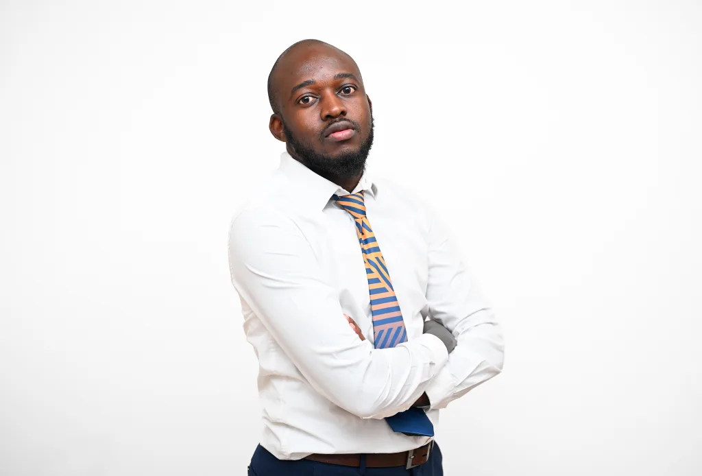 Man in a white dress shirt and orange-blue striped tie with arms crossed, posing against a white background.
