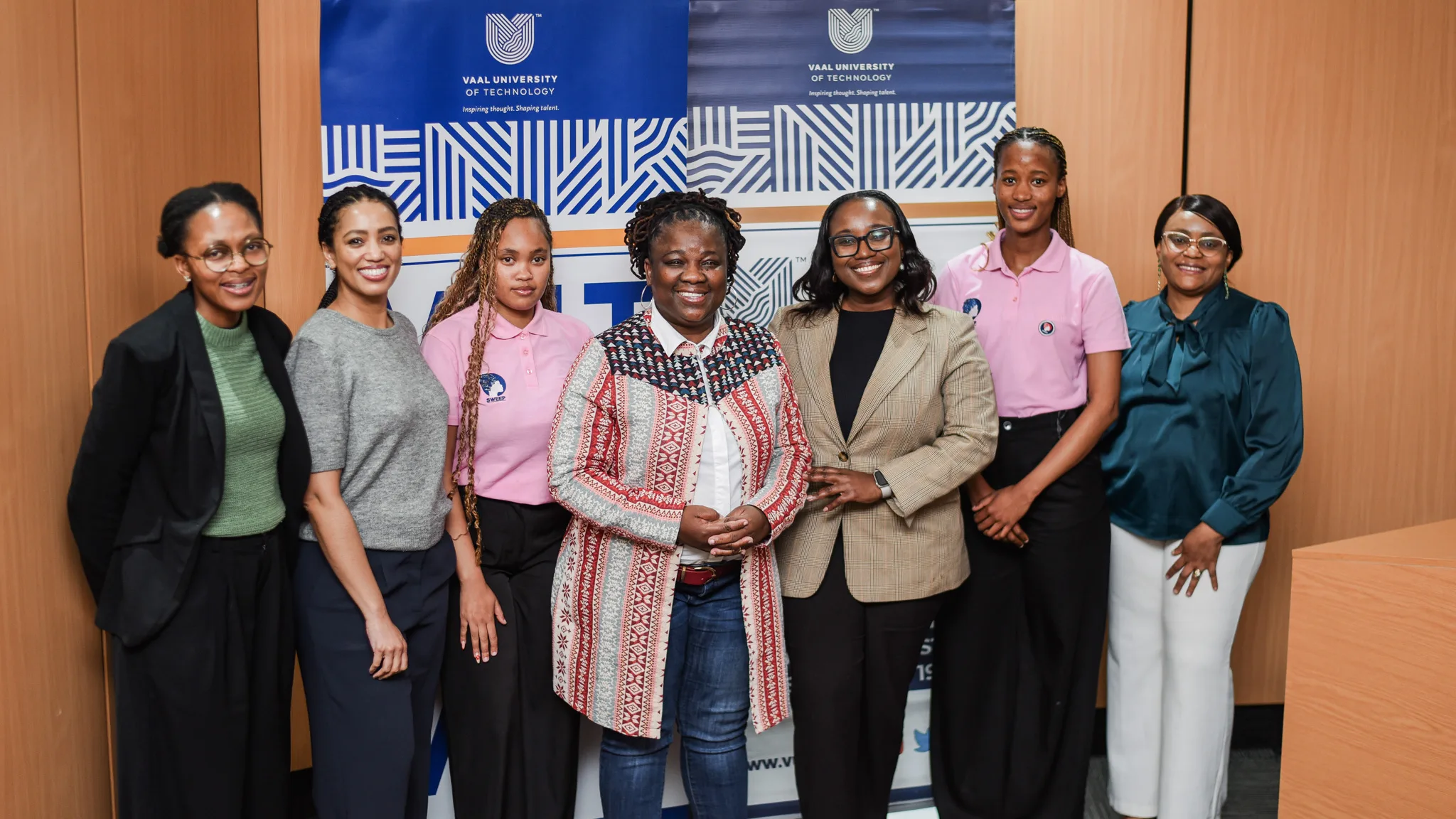Seven women pose for a group photo indoors, with a Vaal University banner in the background.