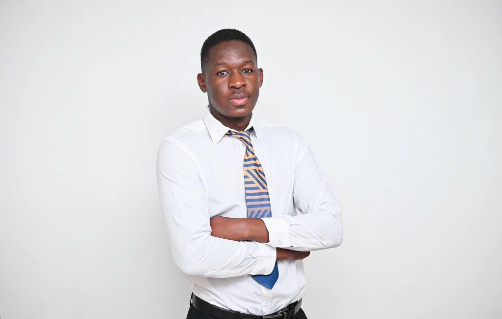 Professional man in a white shirt and orange-blue striped tie, arms crossed, neutral light-gray background.
