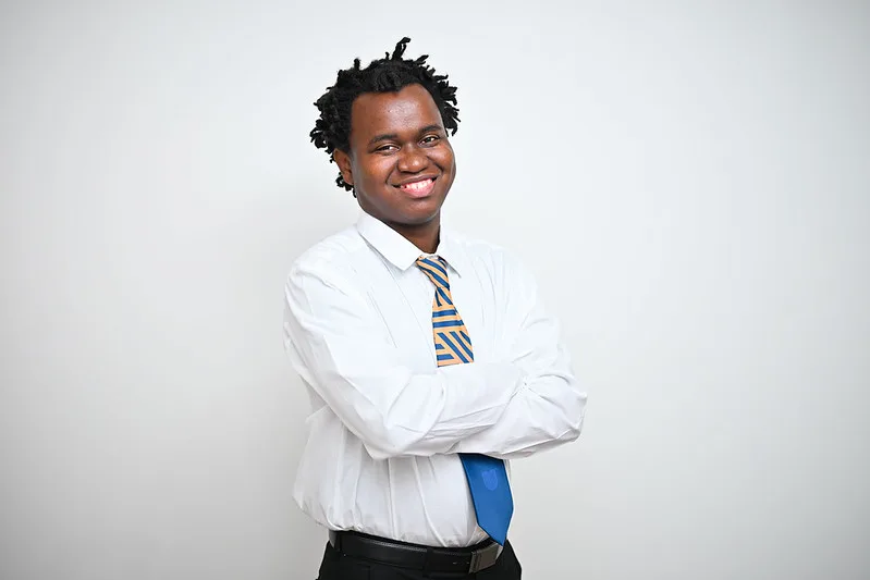 Professional portrait of a smiling man in a white shirt and striped tie, arms crossed, against a light gray background.