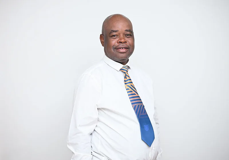 Smiling man in a white dress shirt and blue-yellow striped tie against a plain light backdrop.