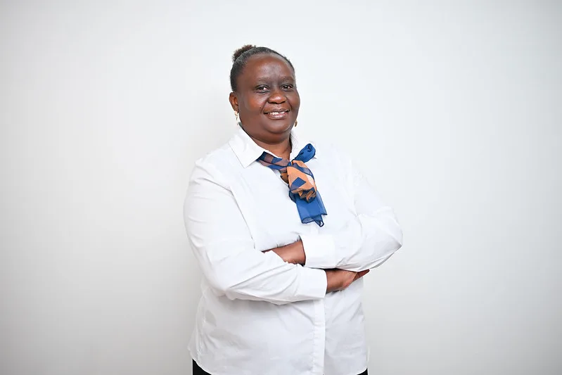 Professional woman with arms crossed, wearing a white blouse and a blue-orange scarf, smiling against a plain light background.