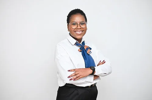 Professional portrait of a smiling Black woman in a white blouse with a blue scarf, glasses, and crossed arms.