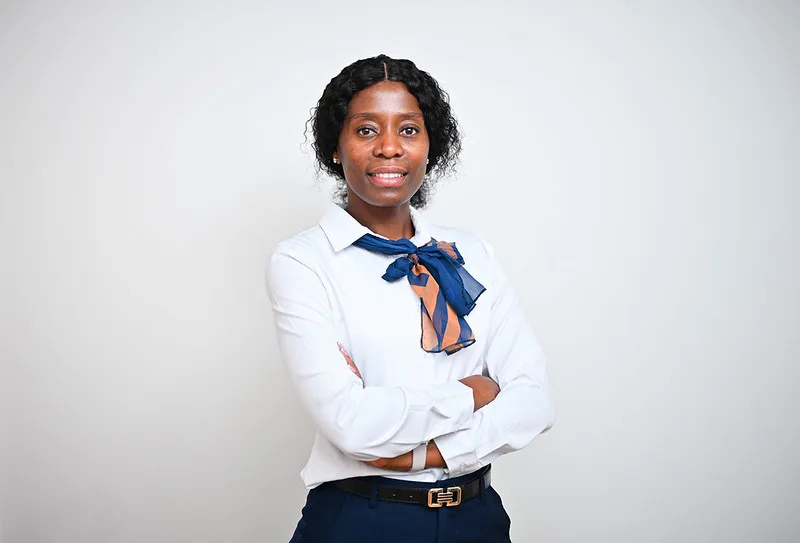 Professional woman with arms crossed, wearing a white blouse and blue scarf, smiling at the camera.