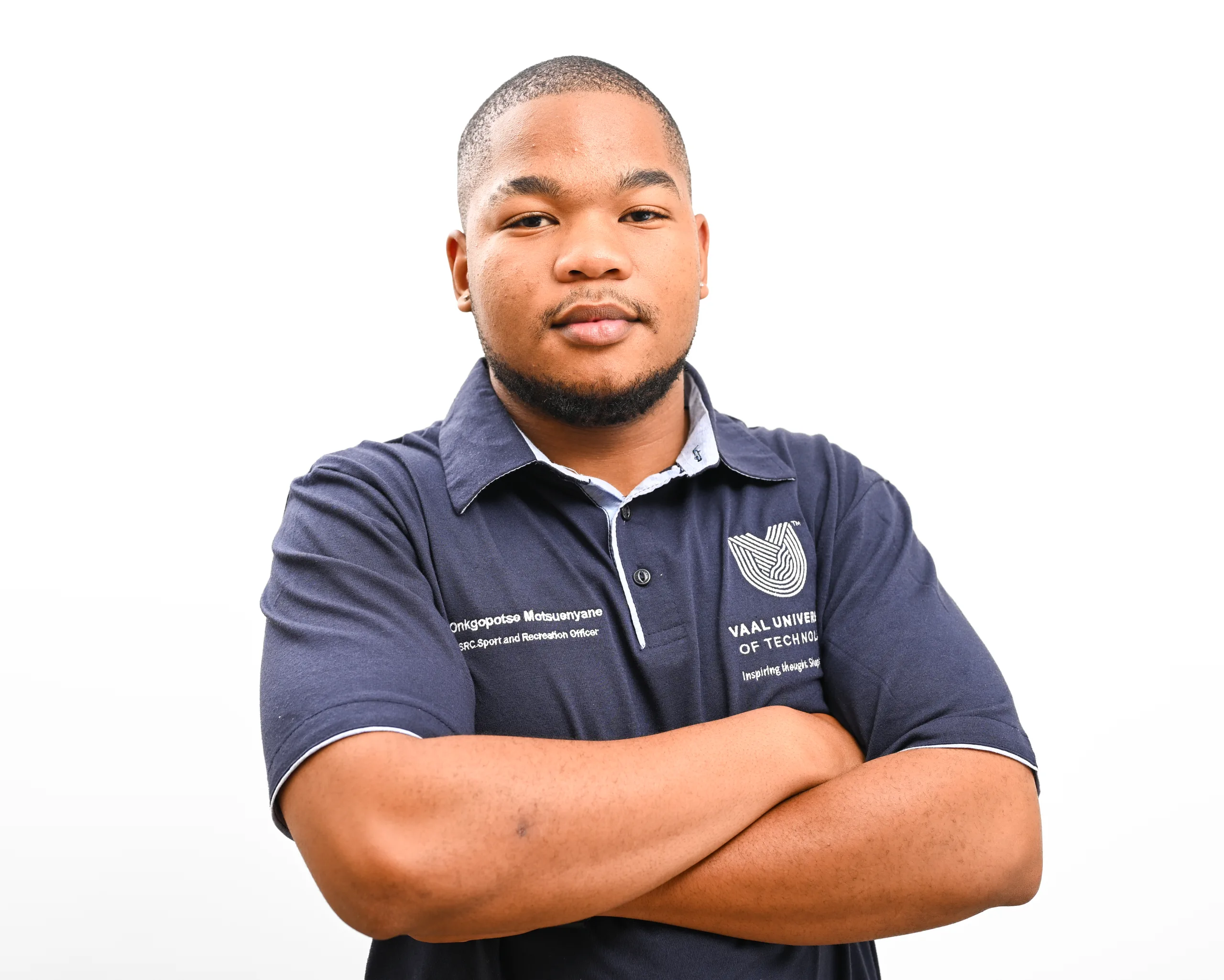 Portrait of a man with arms crossed, wearing a navy polo shirt with a crest on a white background.