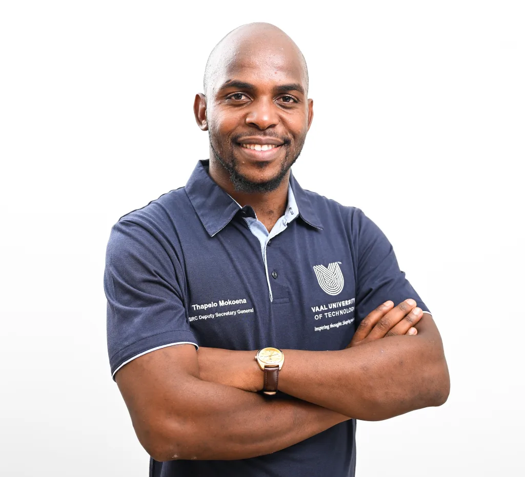 Smiling man with arms crossed, wearing a navy polo shirt with a logo on the chest.