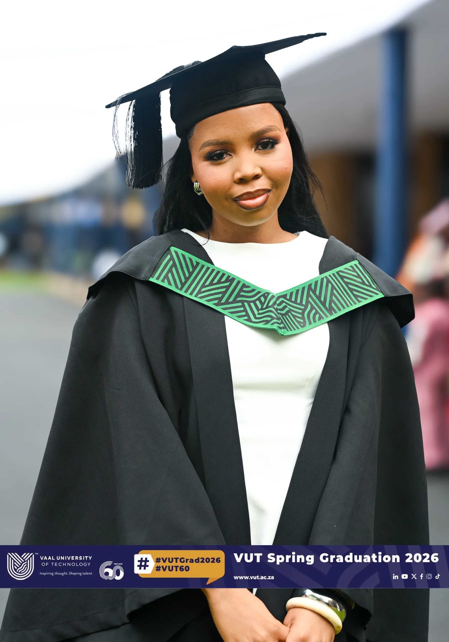 Graduate in cap and gown with a green geometric stole, smiling outdoors; banner shows VUT Spring Graduation 2026 at the bottom.