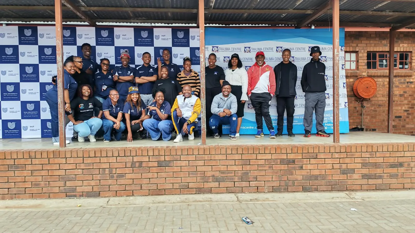 Group of diverse people posing and smiling on a stage with a blue-and-white sponsor backdrop behind them.